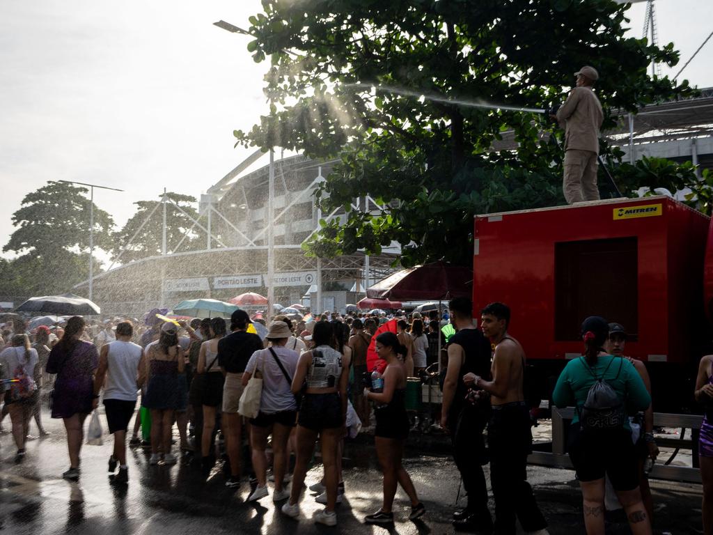 A firefighter cools off fans of US singer Taylor Swift with a hose as they queue outside the Nilton Santos Olympic Stadium. Picture: AFP