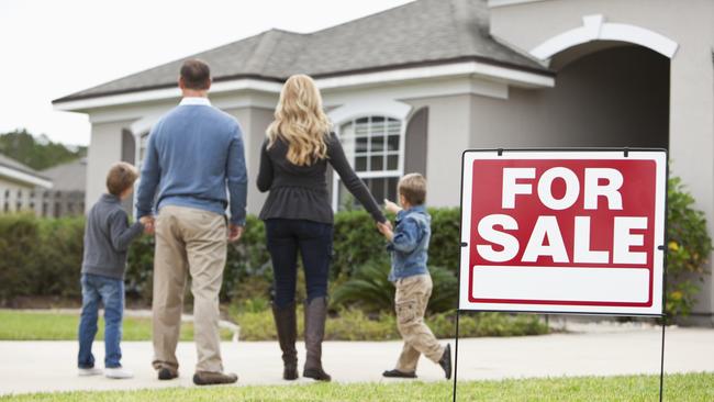 Family with two boys (4 and 6 years) standing in front of house with FOR SALE sign in front yard.  Focus on sign.