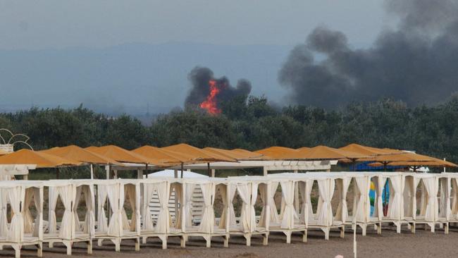 People rest on a beach as smoke and flames rise after explosions at a Russian military air base, in Novofedorivka, Crimea. Picture: Reuters.