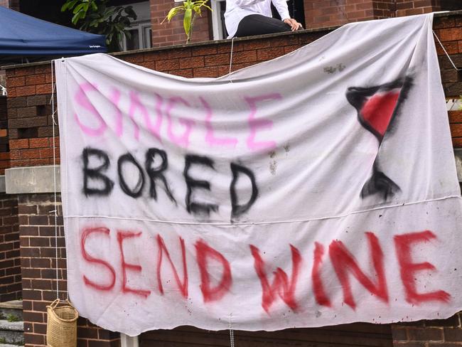 Single, Lonely, Bring wine.  31-year-old eastern suburbs woman Corrine Dodd has painted on an old bed sheet and hung outside her apartment.  She has been gifted a few bottles of wine. She put the sign up for a giggle and make people laugh during the coronavirus crisis. Picture's Darren Leigh Roberts