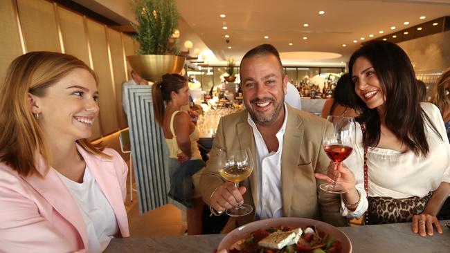 19/10/2018: Hellenika owner Simon Gloftis relaxes with a drink and some food, brought by Assistant Bar Manager Lauren Smith (L), and shares a joke with customer (R) Lisa Ferro, in James St, Fortitude Valley, Brisbane. Hellenika restaurant has just opened at The Calile Hotel, in Fortitude Valley. Lyndon Mechielsen/The Australian