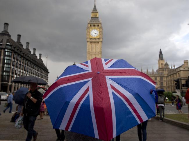 TOPSHOT - A pedestrian shelters from the rain beneath a Union flag themed umbrella as they walk near the Big Ben clock face and the Elizabeth Tower at the Houses of Parliament in central London on June 25, 2016, following the pro-Brexit result of the UK's EU referendum vote. The result of Britain's June 23 referendum vote to leave the European Union (EU) has pitted parents against children, cities against rural areas, north against south and university graduates against those with fewer qualifications. London, Scotland and Northern Ireland voted to remain in the EU but Wales and large swathes of England, particularly former industrial hubs in the north with many disaffected workers, backed a Brexit. / AFP PHOTO / JUSTIN TALLIS