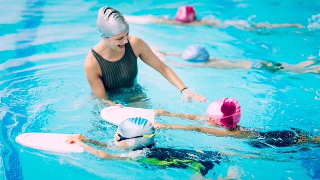 Swim instructor teaching children to swim in pool. Generic.