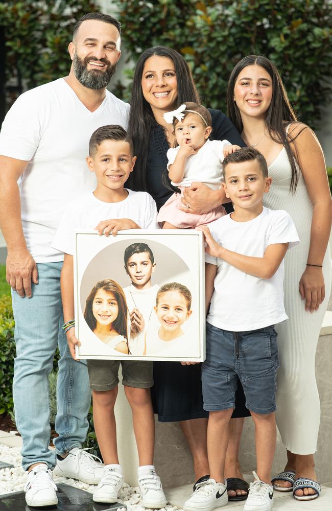 Danny, Leila, Lan, Alex, Michael and Selina Abdallah. They are holding a photograph of Anthony, 13, Angelina, 12, and Sienna Abdallah, 8.