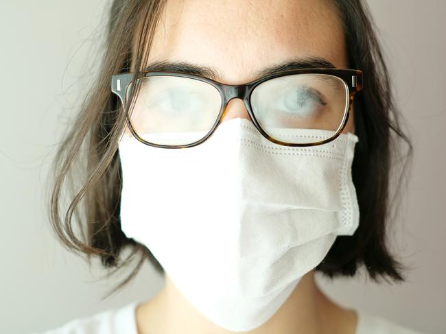 Close up of a caucasian woman wearing a white face mask during coronavirus outbreak with her glasses foggy from breath; mask problems