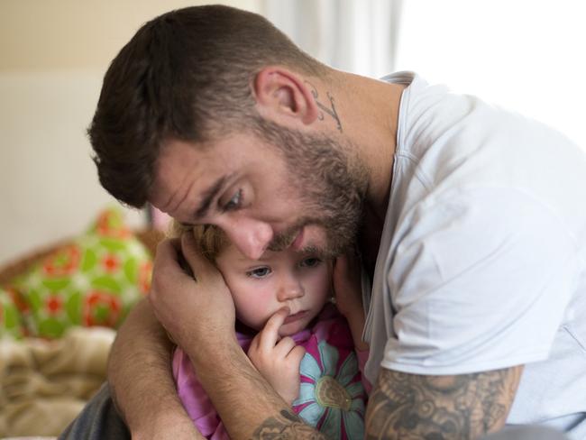 A father comforts his upset little girl, he hugs her tightly. The little girl looks upset and tired.