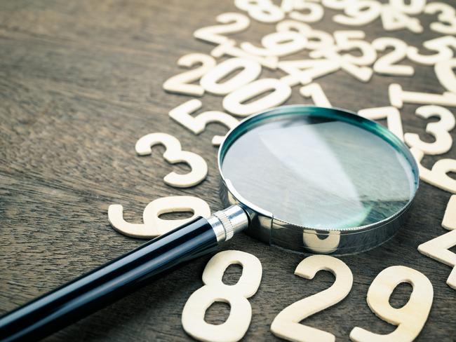 Closeup magnifying glass in scattered numbers on wood background, calculation, mathematics concept