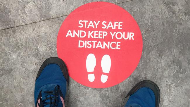 A sign on the floor of a shop, advising customers regarding social distancing guidelines.