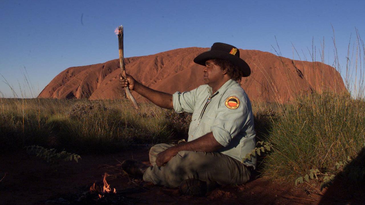 Aboriginal elder Rupert Goodwin holds a traditional firestick in front of Uluru. No campaigners are calling for a treaty to address land rights and more.