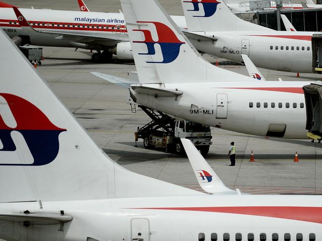 Malaysia Airlines ground staff walk past Malaysia Airlines aircraft parked on the tarmac at the Kuala Lumpur International Airport in Sepang on June 20, 2016. Malaysia is hosting a two-day meeting with Australia and China to discuss next steps in the fruitless search for missing Malaysia Airlines flight MH370. / AFP PHOTO / MANAN VATSYAYANA