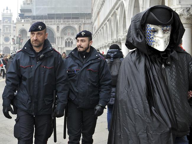 A mask crosses St. Mark's Square as police officers patrol on the occasion of the Venice Carnival, in Venice, Italy, Saturday, Jan. 30, 2016. People attended the Venice Carnival, celebrated Saturday under heightened security following the sexual assaults on New Year's Eve in Cologne and the ongoing terror threat in Europe. Authorities have increased surveillance throughout the city, including the number of officers on patrol, both under-cover and in uniform. (AP Photo/Luigi Costantini)