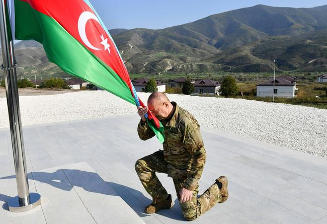 Handout from Azerbaijani presidential press office showing Aliyev kneeling by an Azerbaijani national flag in Khojaly, Nagorno-Karabakh