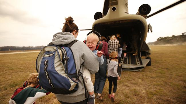 Evacuees are flown out of Mallacoota Airport by an ADF chinook helicopters, the noise and heat from the turbine engines terrifying a young child. Picture: David Caird