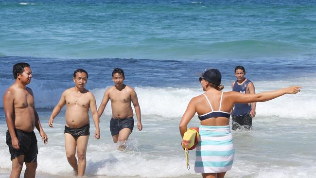 Lifeguards at Surfers Paradise beach keep an eye on beachgoers and keep them swimming between the flags on one of the busiest days of the year. A Lifeguard moves four Burmese men back to the flagged area. Picture: Glenn Hampson