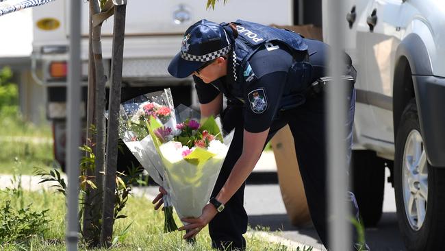 A Police officer places flowers brought over by a neighbour outside a house in Pimpama on the Gold Coast.