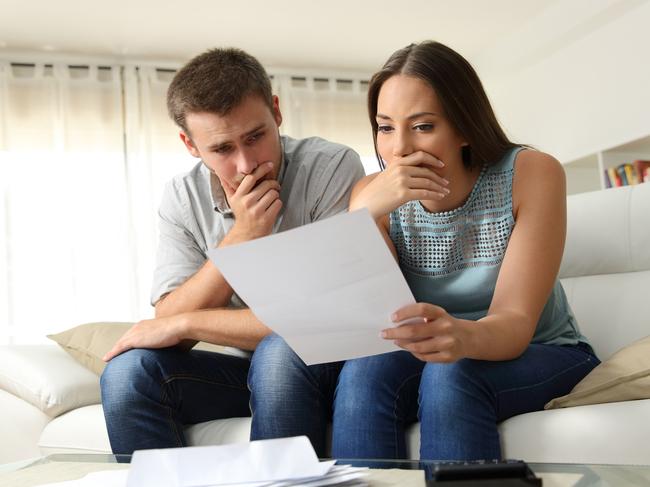 Worried couple reading a letter sitting on a couch in the living room at home