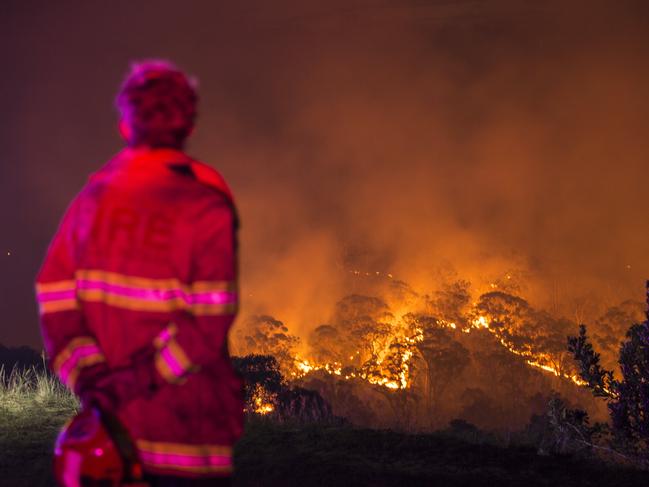 A firefighter waits on a ridge on Royal Oak Drive in the Menai area as a bush fire approaches homes from the other side of the valley. Picture: Damian Shaw