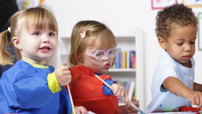 A portrait of a group of  toddlers painting whilt their carer tidies.