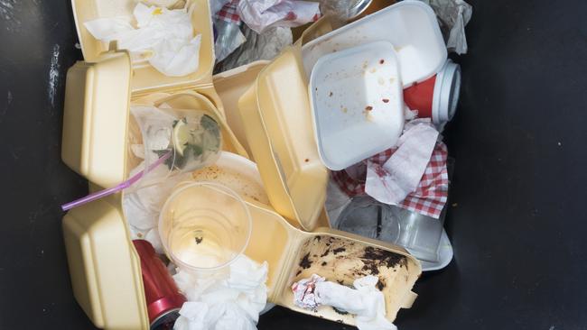 Fast food and drinks containers lying in a heap at the bottom of a garbage bin.