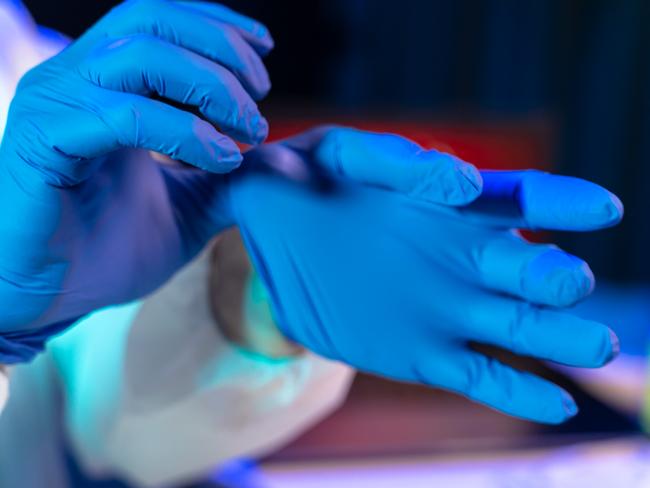 Doctor putting on protective blue surgical gloves. The scene is situated in controlled photography studio environment faking chemical laboratory. Picture is taken with Sony A7III camera.