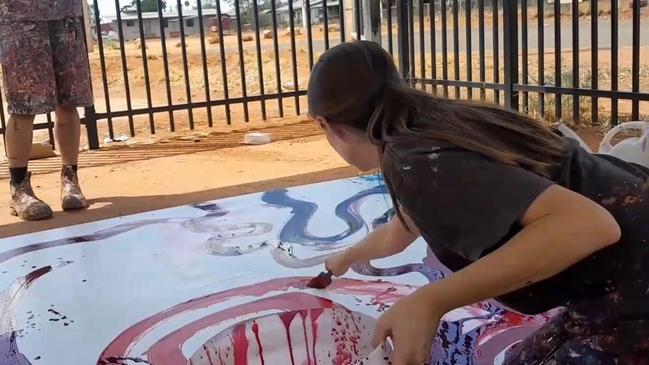 A still image from a video showing Rose Palmer, manager of Tjala Art in the APY Lands settlement of Amata, contributing to a painting by Indigenous artist Yaritji Young.