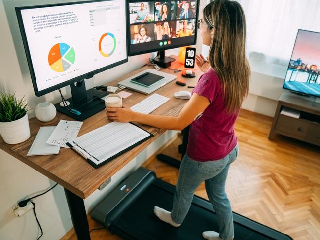 Woman working from home at standing desk is walking on under desk treadmill