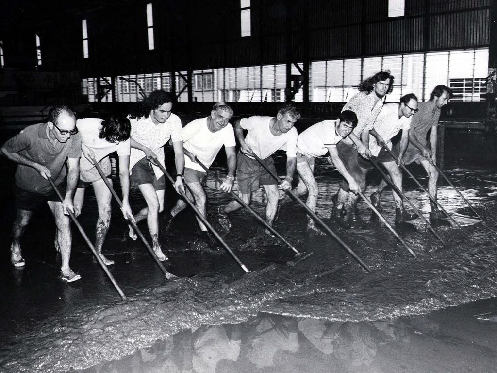 1974 - UK Motors workshop workers sweeping out water and mud from inside the building. Picture: Ted Holliday