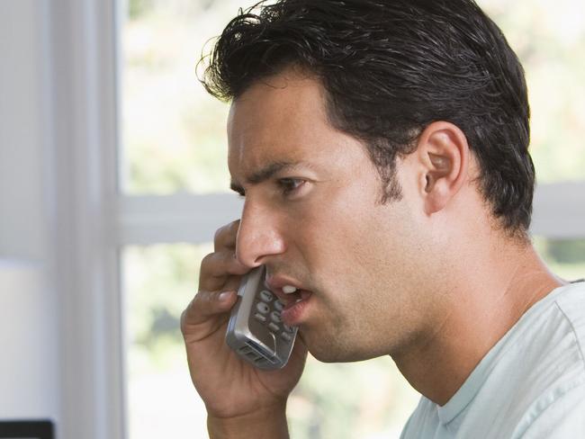 Man in home office on telephone using computer and frowning. For letters page. Computer problem generic