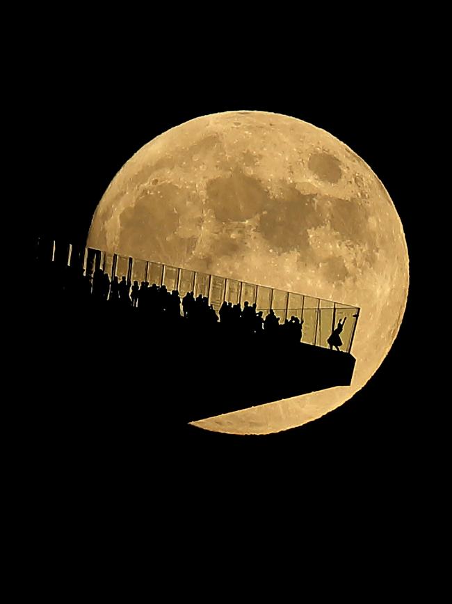 New York photographer Gary Hershorn captured an image of the rising moon behind the Edge observation deck, where Tasmania’s Liza-Jane Sowden just happened to be posing in her Tasmanian tutu. Picture: Gary Hershorn