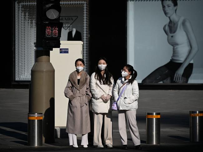 Women wait to cross a street in Beijing. China is now experiencing the planet’s biggest surge in infections. Picture: AFP