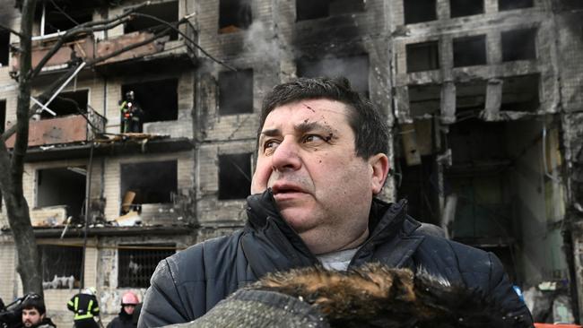 A man holds his dead cat in a blanket as he stands outside a destroyed apartment building in the Obolon district of Kyiv.