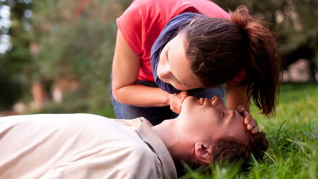 First aid - Look, listen and feel for breathing. Woman is performing first and on a man laying in the grass. She is pulling his head back, listening to his breath and looking at his chest to check if he is breathing. The man is laying unconscious. iStock