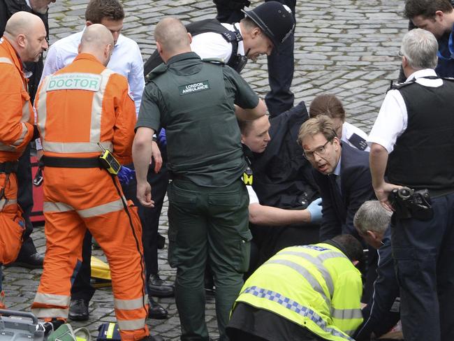 Conservative MP Tobias Ellwood, centre, helps emergency services attend to the police officer outside Parliament. Picture: Stefan Rousseau/PA via AP