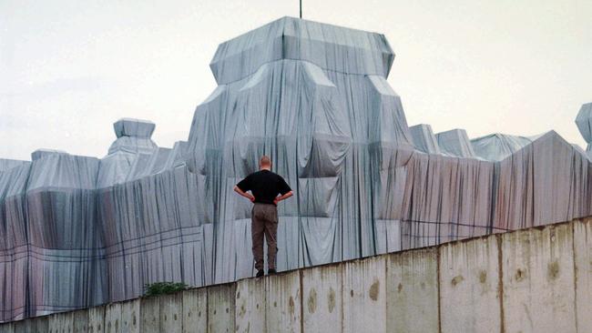 A man on top of remains of the Berlin Wall looks at the wrapped Reichstag building, a project titled Wrapped Reichstag in 1995. Picture: AP