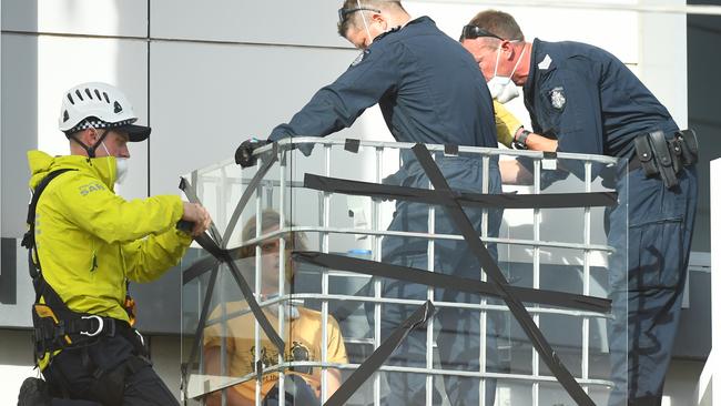 Police officers work to free a refugee rights activist who locked themselves in a cage next to the Mantra Hotel in Preston. Picture: AAP Image/James Ross