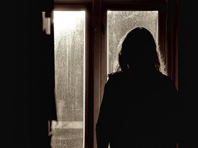 Silhouette of a woman looking through dirty back lit windows one early morning.