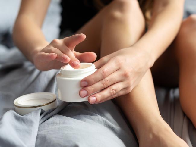 Young woman with cream for feet sitting on bed