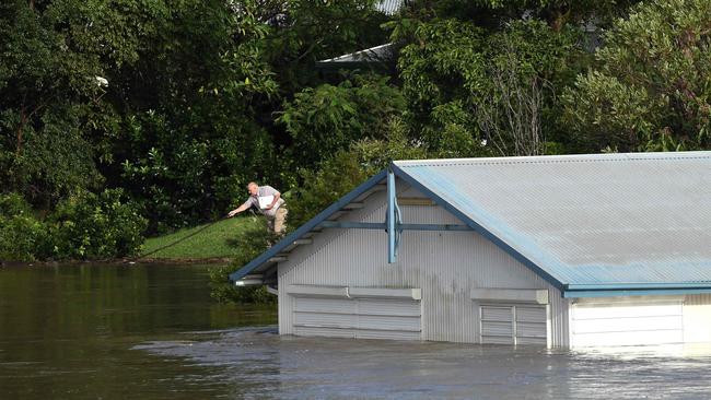 A man pushes away floating debris next to a flooded shed on the bank of over flowing Clarence River in Grafton on March 1, 2022. Photo: SAEED KHAN / AFP