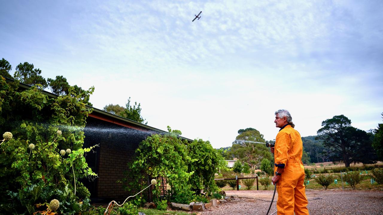 Paul Delaney hoses his property at Mylor as water bombers fly overhead on Monday. Picture: Mike Burton