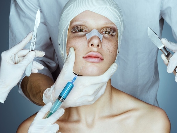 RendezView. Patient in bandages. Nurses holding scalpel and syringe near her face. Plastic Surgery concept. (Pic: iStock)