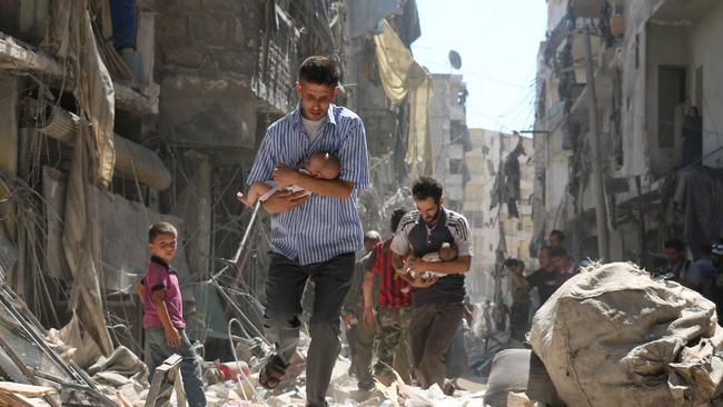 Syrian men carrying babies make their way through the rubble of destroyed buildings following a reported air strike on the rebel-held Salihin neighbourhood of the northern city of Aleppo in September, 2016. Picture: Ameer Alhalbi/AFP Photo