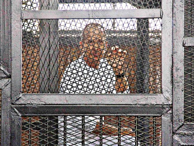 Peter Greste appears in a defendants' cage in the Police Academy courthouse along with several other defendants during a trial on terror charges in Cairo, Egypt. (AP Photo/Hamada Elrasam, File)