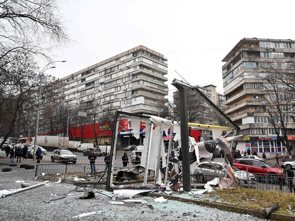 People are seen outside the cordoned off area around the remains of a shell in a street in Kyiv on February 24, 2022.