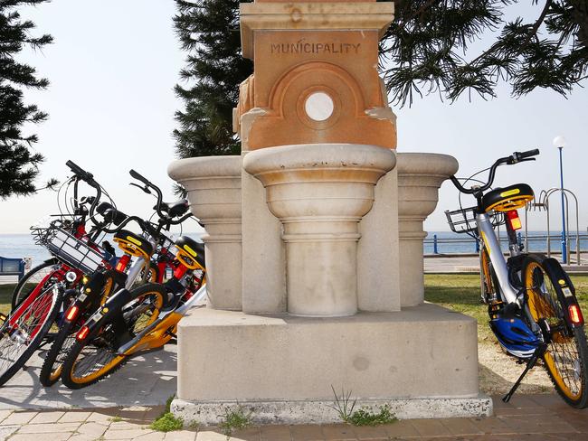 Hire bikes overflow out of a bike rack and are propped up against the historic James Robertson Fountain at Coogee Beach. Picture: John Appleyard