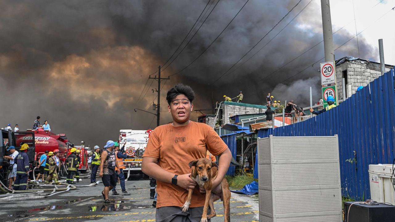 A man carries a dog during a fire away from the flames as homes in Tondo burn. (Photo by JAM STA ROSA / AFP)