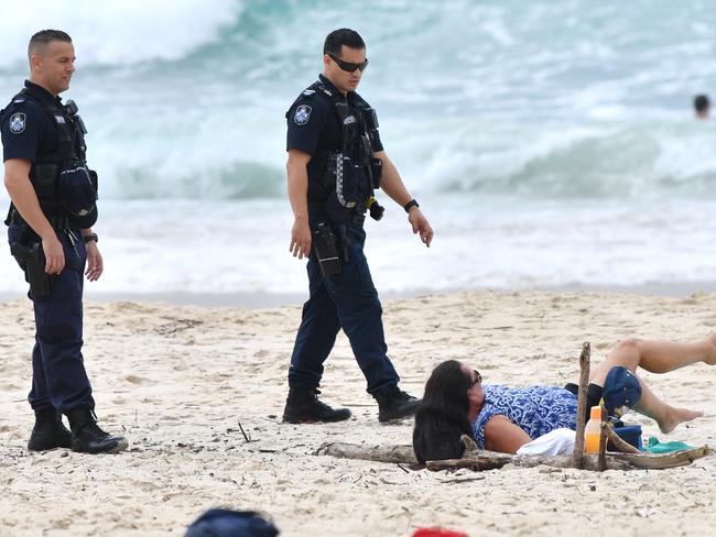 Queensland Police are seen moving on a sunbather from the beach at Burleigh Heads on the Gold Coast. (AAP Image/Darren England)