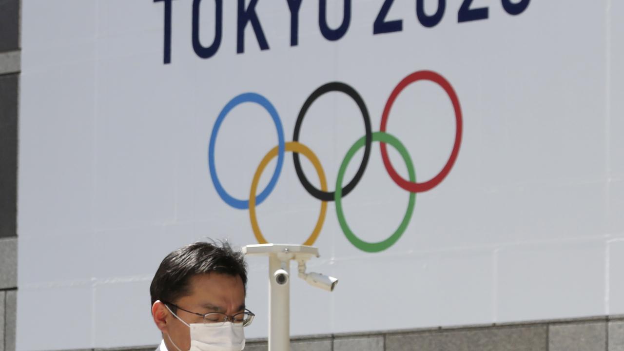 A man walks in front of a Tokyo Olympics logo at the Tokyo metropolitan government headquarters.
