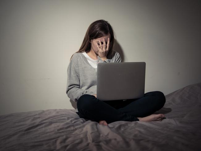 Scared and intimidated sad teenager bullied on line with laptop suffering cyberbullying and harassment. Child victim of bullying stalker social media, online challenges, technology and dangers of internet.