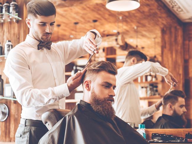 Side view of young bearded man getting haircut by hairdresser while sitting in chair at barbershop. Image: iStock For Study Options 2017 feature