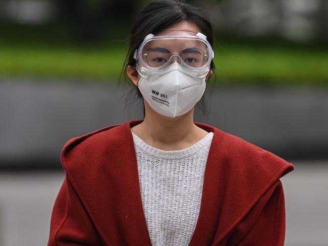 A woman wearing a facemask and googles walks along a street in Wuhan in China’s central Hubei province on April 5, 2020. (Photo by Hector RETAMAL / AFP)